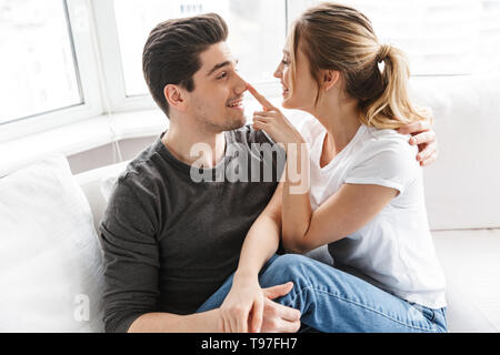Image of positive couple man and woman hugging together while sitting on sofa in bright room at home Stock Photo