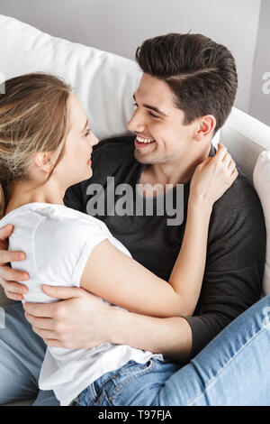 Image of couple in love man and woman hugging together while sitting on sofa in bright room at home Stock Photo