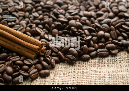 a mountain of whole grains of coffee with cinnamon sticks on the light burlap background with little space for text Stock Photo
