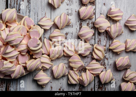 Pink marshmallows with yellow curls, on light wooden background. Poured from the white plate Stock Photo