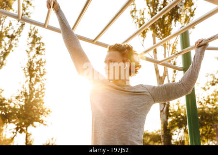 Concentrated young sportsman doing exercises on bars outdoors Stock Photo