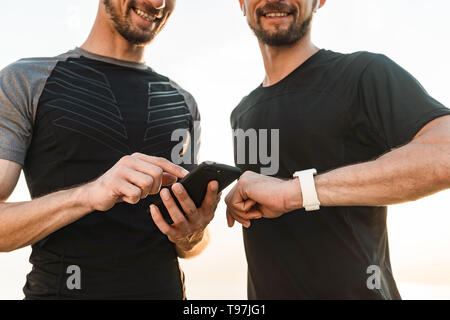 Two twin brothers doing exercises at the beach together, using smart watch Stock Photo
