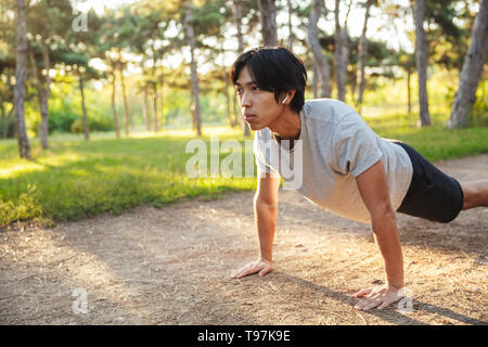 Confident young asian athlete man wearing sportswear doing exercises outdoors at the park, doing plank exercise Stock Photo
