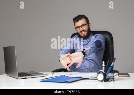 Tired smiling bearded elegant man in eyeglasses warming up while sitting by the table in office Stock Photo