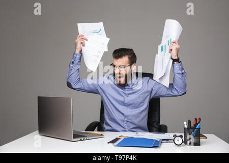 Screaming displeased bearded elegant man in eyeglasses holding documents while sitting by the table in office Stock Photo