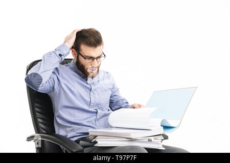Serious shocked bearded elegant man in eyeglasses reading documents while sitting on armchair over grey background Stock Photo