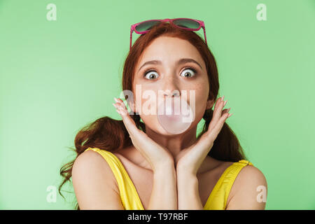 Image of a beautiful young redhead girl posing isolated over green wall background with chewing gum. Stock Photo