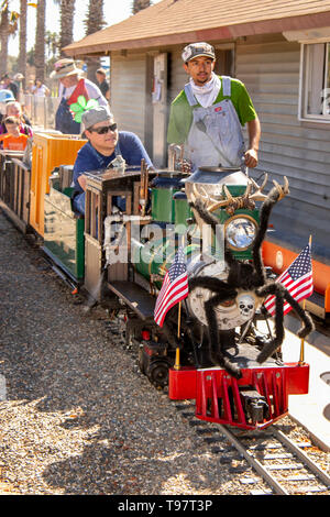 Decorated with antlers and the US flag, a miniature steam locomotive arrives at a station in a Costa Mesa, CA, park. Stock Photo