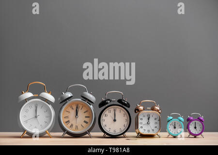 Different alarm clocks on wooden table against grey background Stock Photo