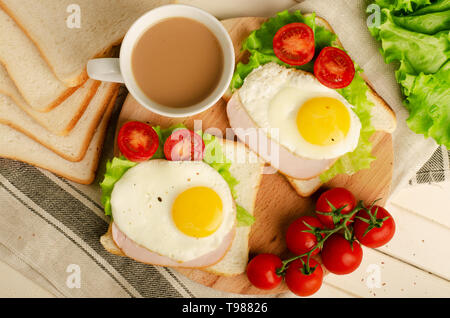 Ham sandwich with scrambled egg, tomato, lettuce, delicious healthy breakfast and coffee on white wooden background Stock Photo