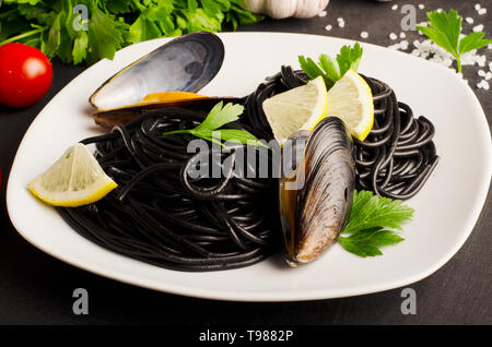 Seafood black pasta spaghetti with mussels on white plate on dark background.  Mediterranean delicacy food Stock Photo