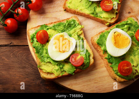 Toasts with avocado, сherry tomatoes and eggs on rustic wooden background Stock Photo
