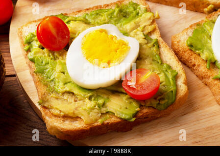 Sandwich with avocado, poached eggs and wholegrain bread on cutting board Stock Photo