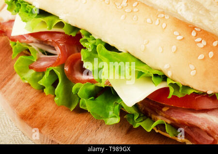 Large subway baguette sandwich cut in half filled with bacon, cheese, lettuce and tomatoes on a cutting board closeup Stock Photo