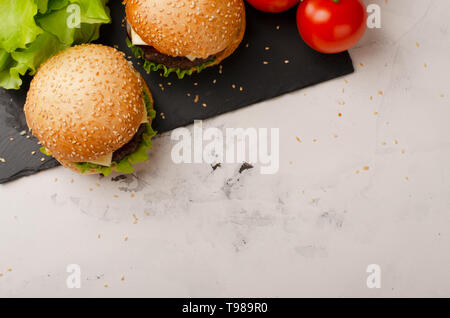 Two homemade beef burgers with red onion, tomatoes and salad on cutting board with space for text. Top view. Stock Photo