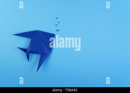 Origami tropical fish on sky blue minimalistic background. Paper sea fish and bubbles under water backdrop concept. Hobby, leisure, pastime. Underwater life, fauna creative craft work flat lay Stock Photo