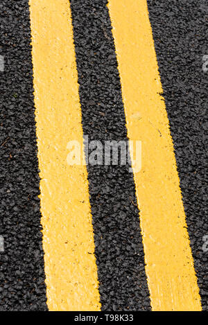 Freshly painted double yellow lines on new black tarmac road surface. No parking warning lines on fresh asphalt. Lined highway Stock Photo