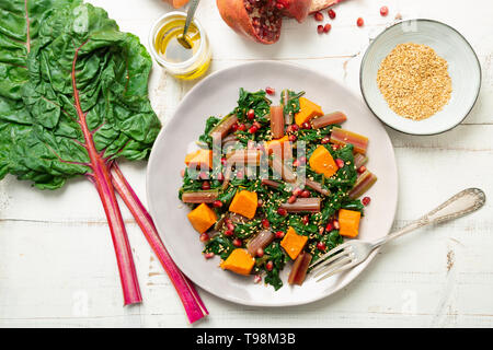 Boiled swiss chard with sweet potato, pomegranate and sesame seeds on a white wooden background. Top view Stock Photo