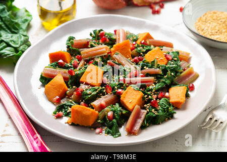 Boiled swiss chard with sweet potato, pomegranate and sesame seeds on a white wooden background Stock Photo
