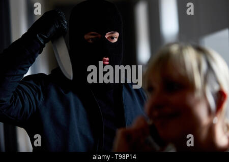 Robber threatens wife at home with a big knife Stock Photo