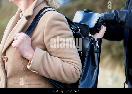 Thief secretly steals purses from a woman's handbag Stock Photo