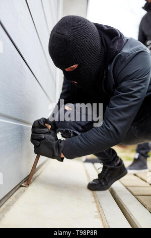 Burglar with crowbars at the gate of a garage or warehouse Stock Photo