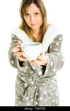 Blonde woman in gray dressing gown with white dots offers white mug with gray dots - focus on coffee or tea - white background Stock Photo
