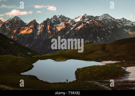 Hikers at Koruldi Lakes look out on the mountains of the Great Caucasus in the evening light, Upper Svanetia, Georgia Stock Photo