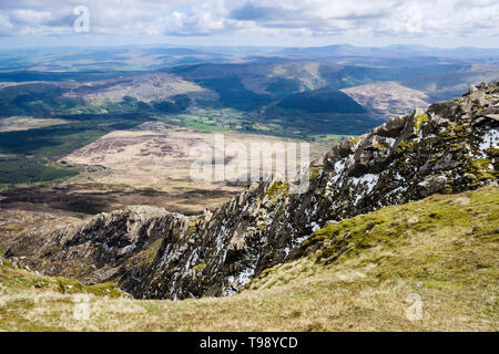 Looking down Daear Ddu rocky east ridge rock scramble with bits of snow and hikers on Carnedd Moel Siabod mountain in Snowdonia National Park Wales UK Stock Photo