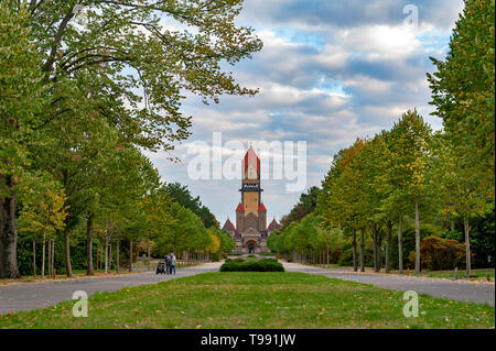 Walkway in beautiful park toward chapel complex, bell tower, funeral hall, and crematorium of Leipzig South Cemetery in Leipzig, Germany Stock Photo