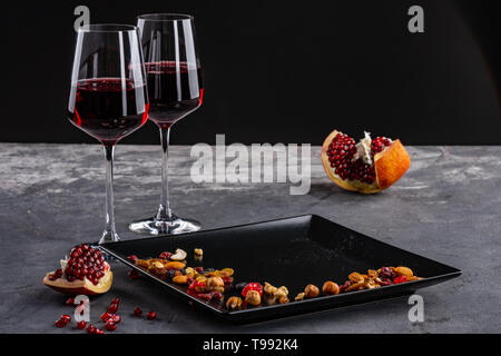 two Glasses of red wine with pomegranate fruit and nuts. stone grey table, dark background. Stock Photo
