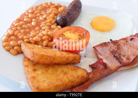 A full English breakfast comprising egg, beans, sausage, hash browns, bacon, and tomato. Stock Photo