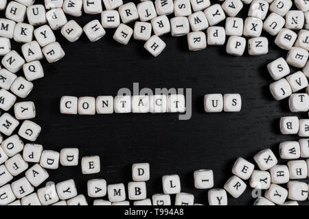 Word CONTAKT US on wooden cubes on a black wooden table with copy space Stock Photo