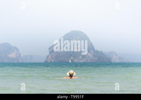 Woman in straw hat swiming in the sea in Krabi Railey beach overlooking the harbour and mountains, Thailand. Stock Photo