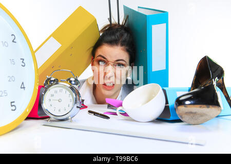 Seriously. Young woman getting a lot of work and deadline, being under the pressure of the deals. Pressed by folders with papers. Concept of office worker's troubles, business, problems and stress. Stock Photo