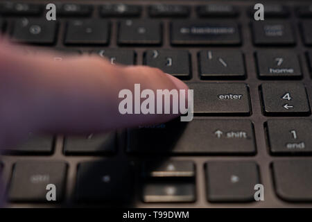 human finger that is pressing the enter key on a computer keyboard Stock Photo