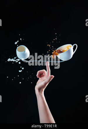 Cup of coffee and a small jug of milk balancing on a long spoon on the tip of a finger. Barista making a balanced latte. Creative coffee concept on a  Stock Photo