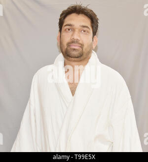 An attractive Asian young man in white terry bathrobe. Man in terry bathrobe isolated on white. Stock Photo