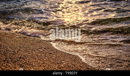 Close-up view of pebble beach at sunset, sun reflects on the water surface Stock Photo