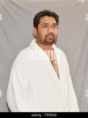 An attractive Asian young man in white terry bathrobe. Man in terry bathrobe isolated on white. Stock Photo