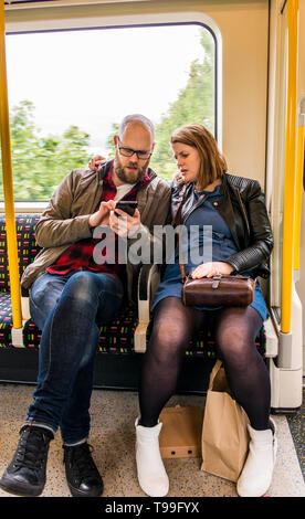 Heterosexual couple on tube train, sitting together, looking at man's smartphone Stock Photo