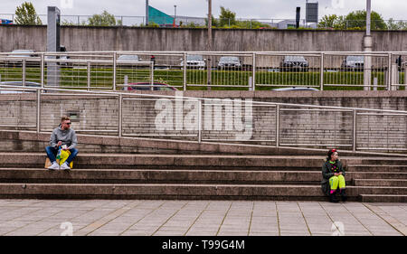 Man and woman sitting on steps, man looking towards woman, large space between them, Quayside, Newcastle upon Tyne, England, UK Stock Photo