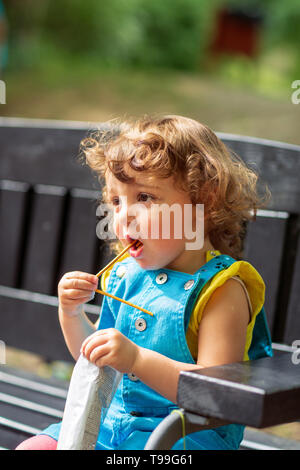 Cheerful cute kid girl eats snacks in park Stock Photo