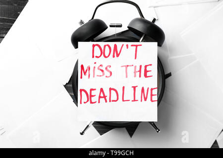 Paper with text DONT MISS THE DEADLINE and alarm clock on table Stock Photo
