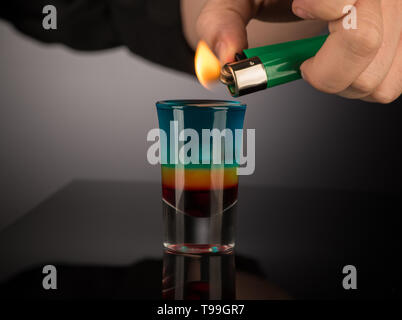 bartender sets fire to a mixed alcoholic cocktail in a shot glass, close-up Stock Photo