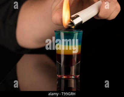 bartender sets fire to a mixed alcoholic cocktail in a shot glass, close-up Stock Photo