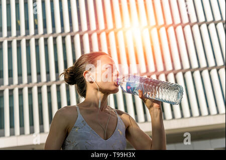 sporty woman drinking water from a bottle, rehydrate after exercise. Stock Photo