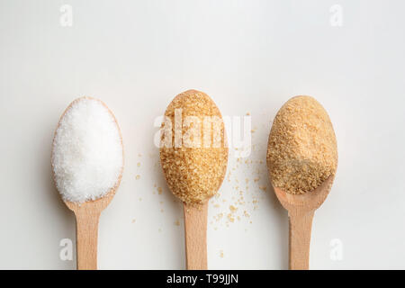 Different granulated sugar in wooden spoons on white background Stock Photo