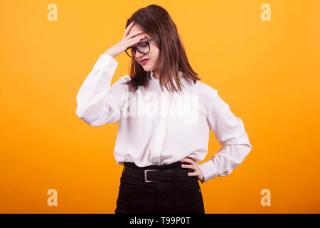 Beautiful teenage girl having a migraine in studio over yellow background. Pretty young girl with serious headache. Stock Photo