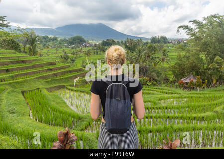 Caucasian female tourist wearing small backpack looking at beautiful green rice fields and terraces of Jatiluwih on Bali island Stock Photo